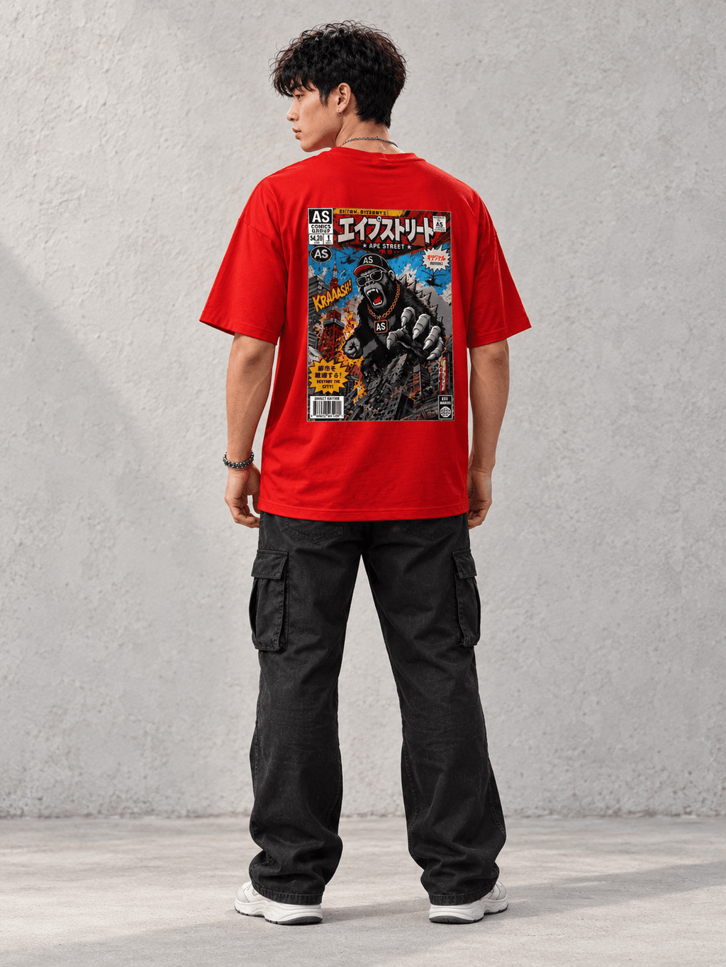 Model wearing Ape Street Apezilla Comic Book Tee, back view showing the back print, against a light concrete backdrop.