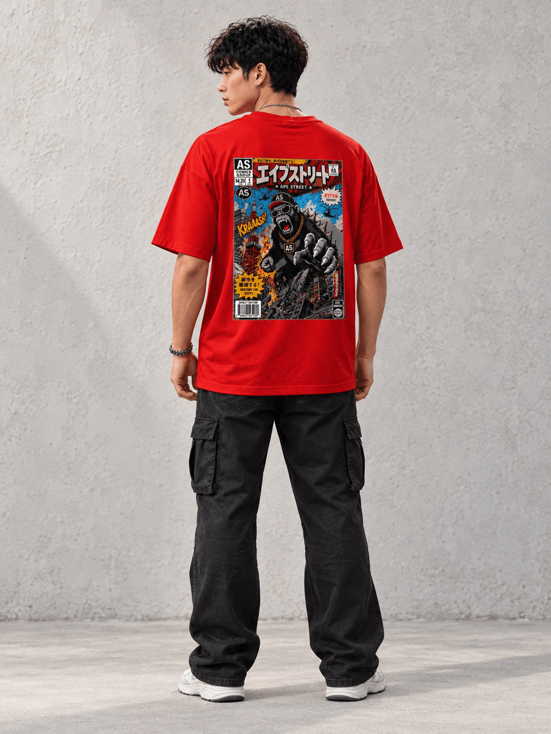 Model wearing Ape Street Apezilla Comic Book Tee, back view showing the back print, against a light concrete backdrop.