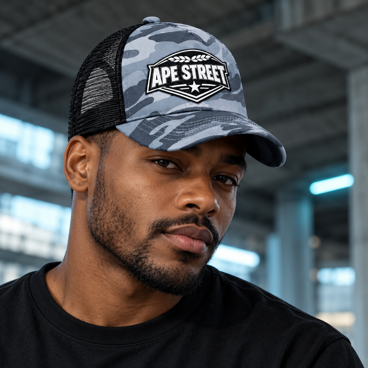 Model wearing the Ape Street grey camo trucker cap in a concrete urban setting