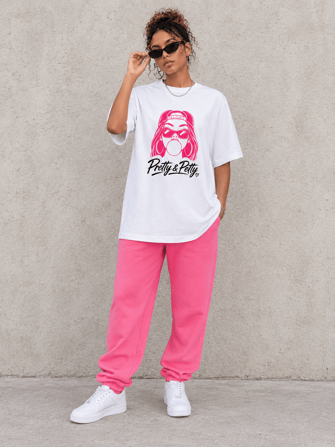 Model wearing Moda Originals Pretty & Petty Pink Tee, front view showing the design, against a light concrete backdrop.