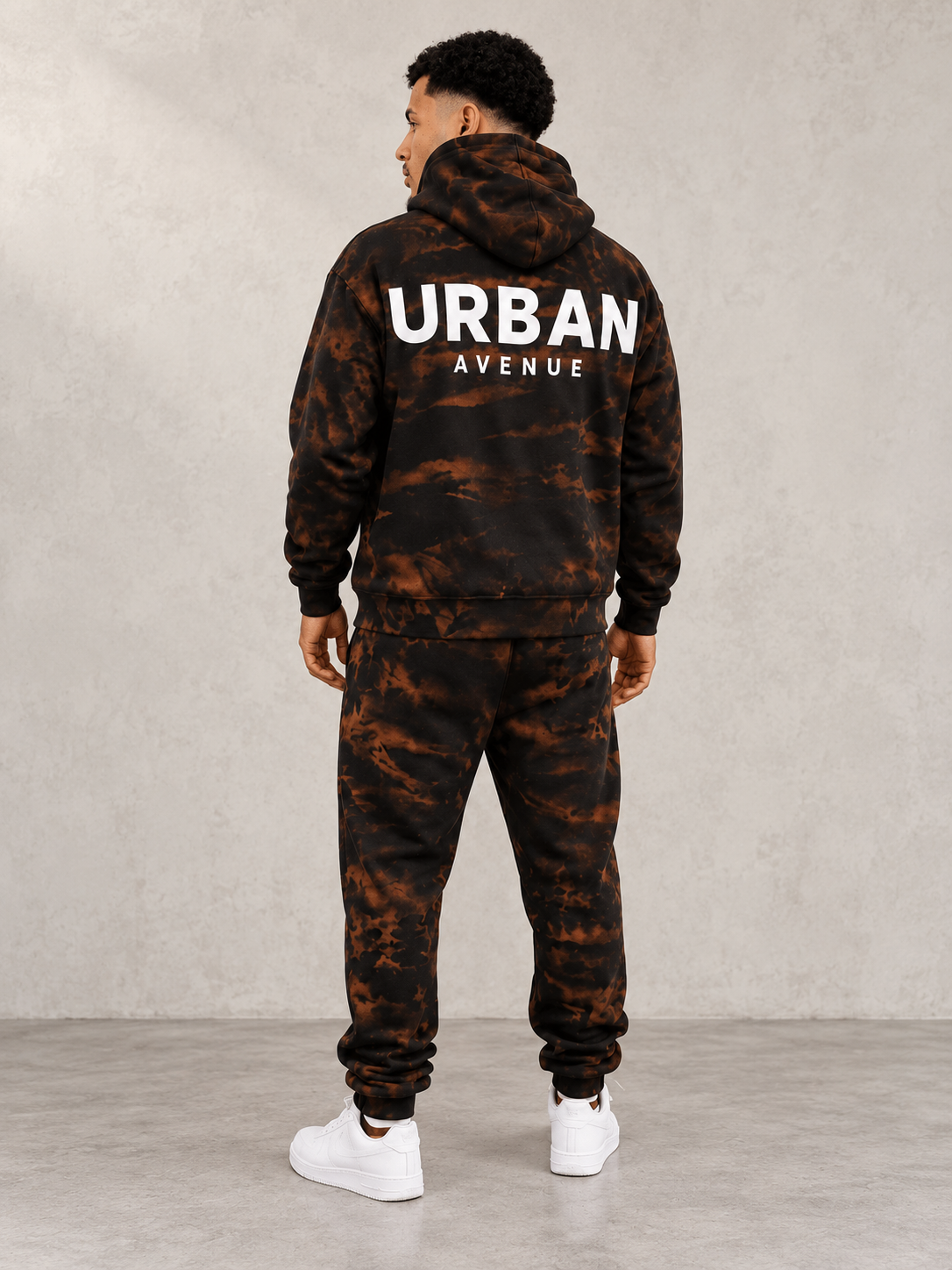 Model wearing Urban Avenue Bleach Wash Tracksuit, back view showing the back print, against a light concrete backdrop.