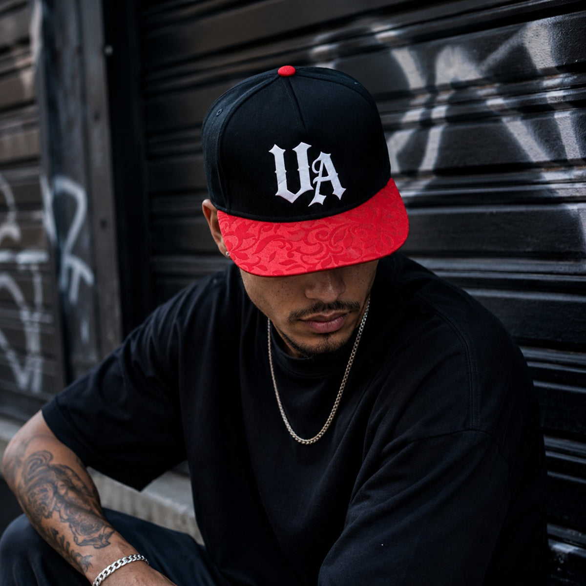 Model wearing Urban Avenue black and red UA cap against a shutter.
