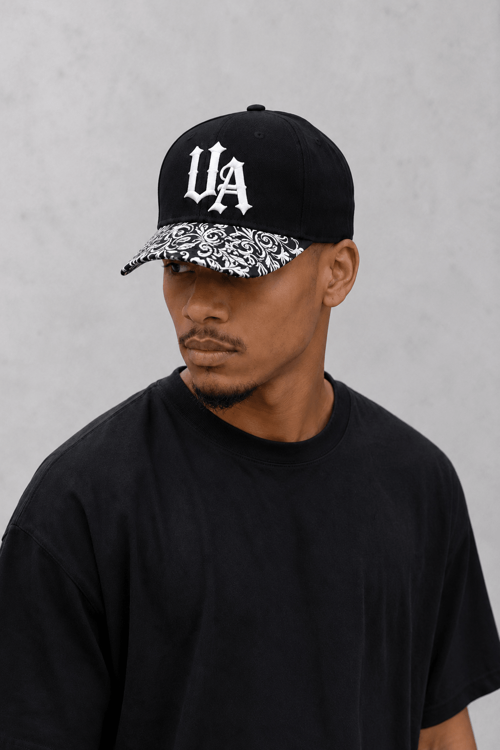 Model wearing Urban Avenue UA baseball cap in black and white against a light grey catalogue background.