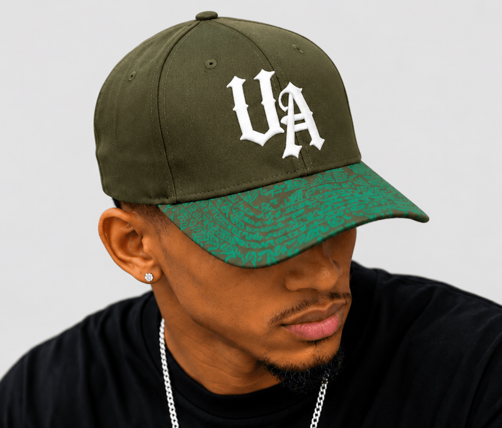 Model wearing Urban Avenue khaki baseball cap with white UA logo and green patterned peak against a light grey background.