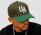 Model wearing Urban Avenue khaki baseball cap with white UA logo and green patterned peak against a light grey background.