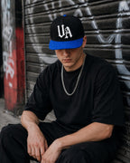 Model wearing Urban Avenue UA Logo Snapback in black and blue against a shutter.