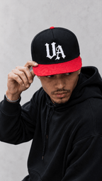 Model wearing Urban Avenue UA Logo Snapback in black and red against a light grey catalogue background.